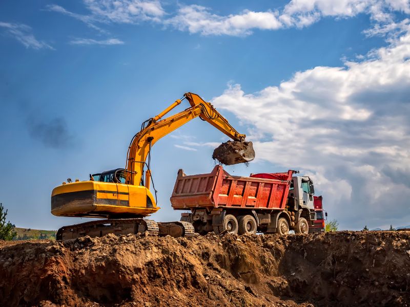 Excavator loading dirt into a dump truck at a job site – commercial auto insurance for construction vehicles Excavator loading dirt into a dump truck at a job site – commercial auto insurance for construction vehicles